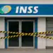 Fachada de agência do INSS fechada com fitas amarelas e pretas de interdição em 2026.