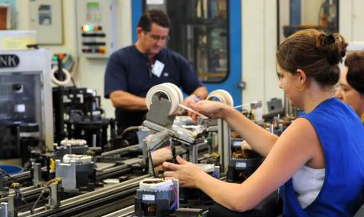 Funcionários operam máquinas em linha de produção industrial em 2026