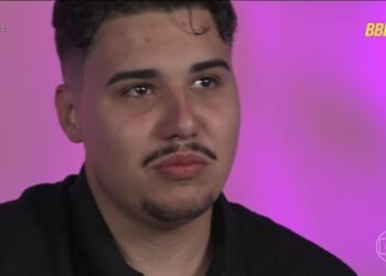 Close do rosto de Pedro, participante do BBB 26, com expressão séria e pensativa, em frente a um fundo rosa vibrante com os logotipos oficiais do programa no canto superior e inferior direito.