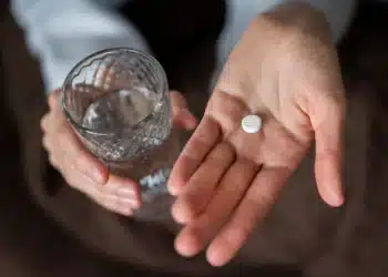 Pessoa segurando pílula e copo de água, com foco no medicamento para queima de gordura.