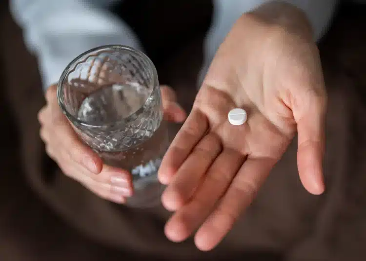 Pessoa segurando pílula e copo de água, com foco no medicamento para queima de gordura.