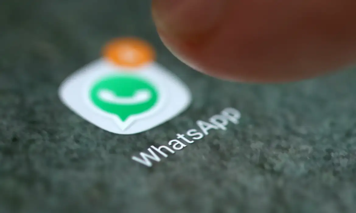  Tela de celular com ícone do WhatsApp e notificação laranja, acompanhado por dedo próximo ao ícone