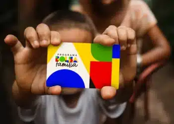 Criança segurando cartão do Bolsa Família colorido em primeiro plano