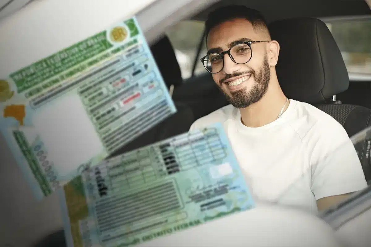  Homem sorrindo mostra carteira de motorista dentro do carro.