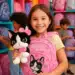 Menina segurando mochila rosa com desenho de cachorro e pelúcia combinando em loja de mochilas infantis.