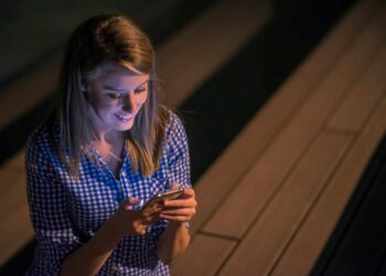 Mulher sorridente em camisa xadrez digitando no celular iluminado à noite