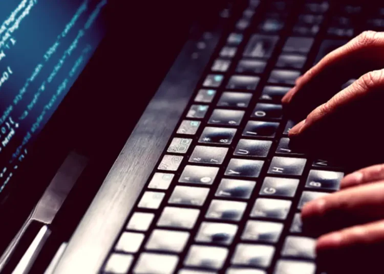 Alerta de golpe: criminosos exigem depósitos antecipados para liberar falsos valores judiciais. Imagem mostra mãos digitando em um teclado de notebook, enquanto a tela exibe códigos de programação iluminados, reforçando o caráter digital do golpe.