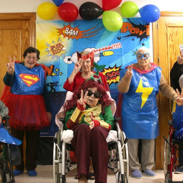 Grupo de idosos vestidos como super-heróis posando e fazendo sinal de paz em festa decorada