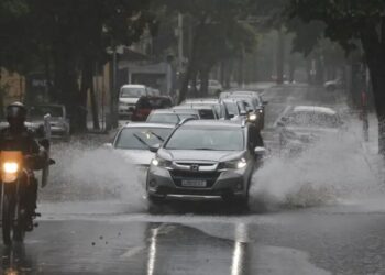 Carros trafegam por rua alagada durante chuva intensa após alerta do Inmet para temporais no Norte e Nordeste.