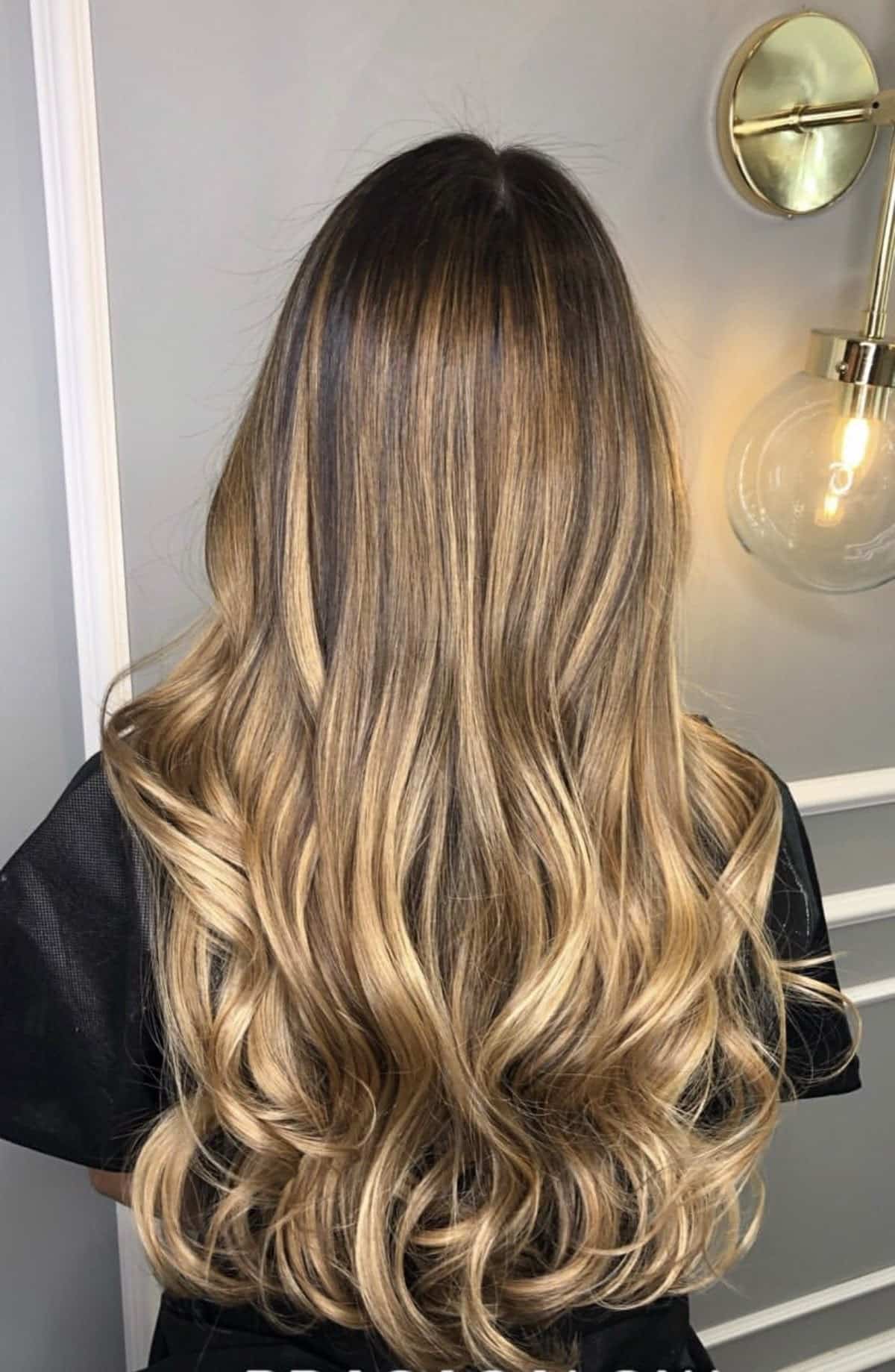 Cabelo longo com mechas loiras onduladas visto de costas sob luz dourada ambiente