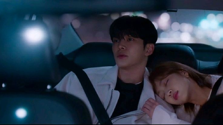 Jovem sentado no banco traseiro do carro com mulher dormindo sobre seu ombro e luzes urbanas ao fundo