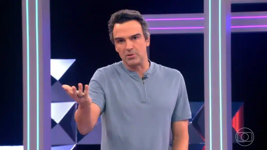 Apresentador gesticulando com uma mão estendida durante fala em estúdio iluminado