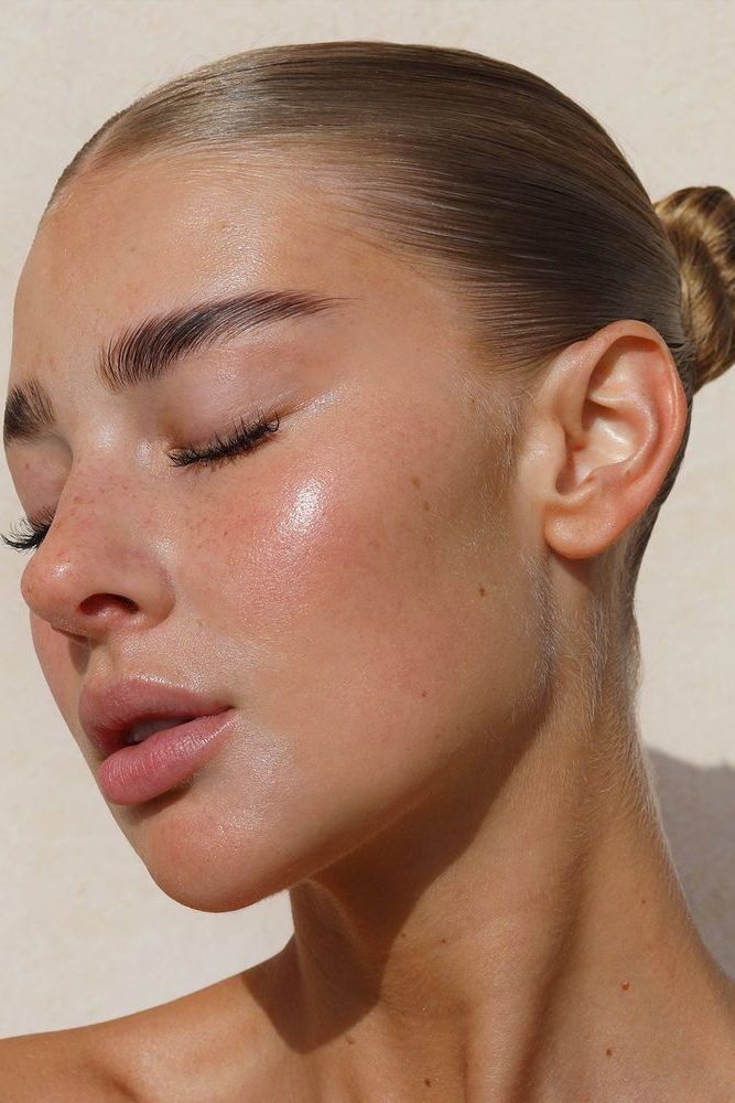 Rosto feminino com pele brilhante e cabelo preso, olhos fechados, evidenciando glow natural