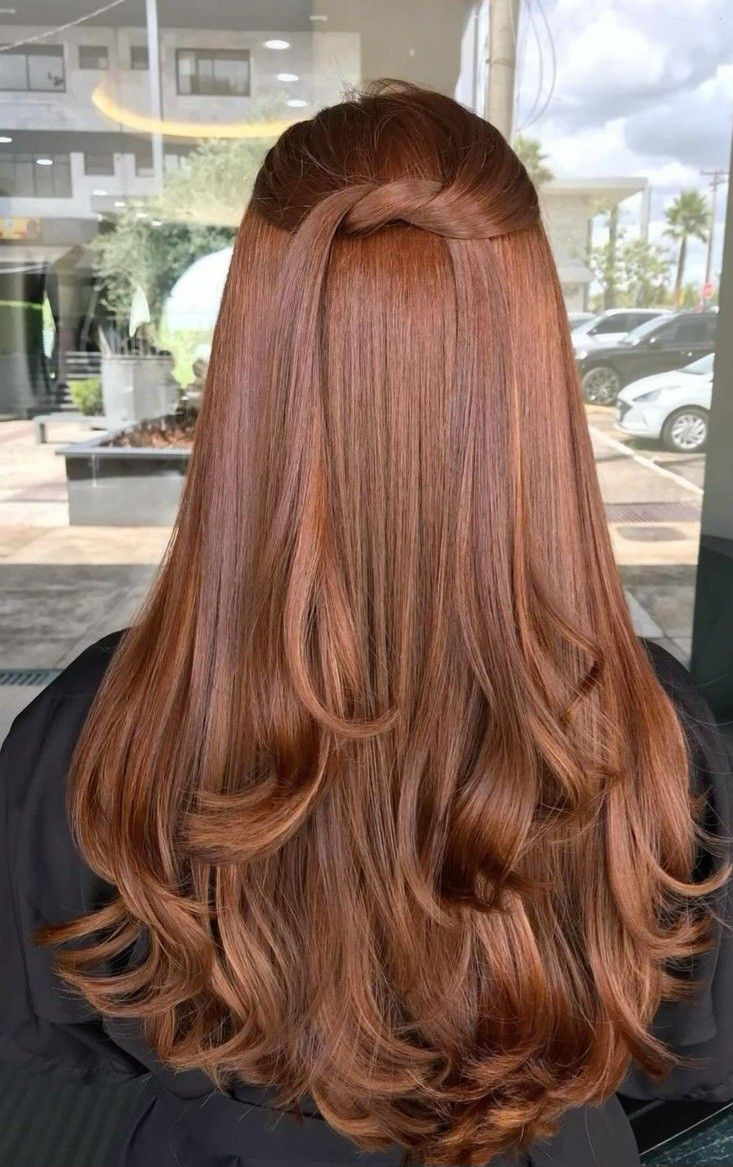 Cabelos femininos ondulados com mechas marrom acobreado vistos de costas em ambiente de salão.