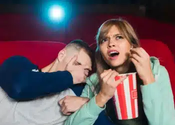 Casal assistindo filme em cinema com luz projetada na tela.