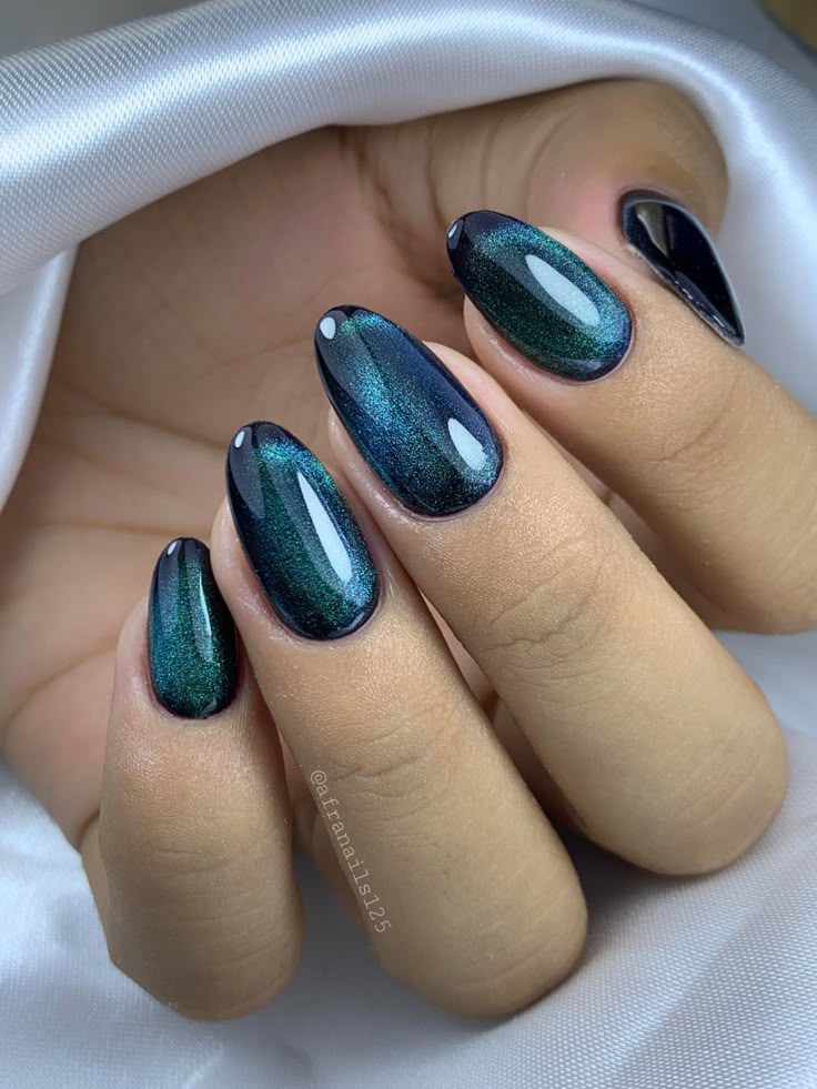 Mão com unhas ovais pintadas com esmalte magnético verde e azul sobre tecido branco.