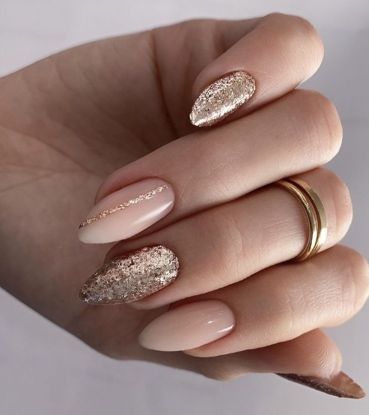 Mão exibe unhas alongadas com esmaltação nude e detalhes em glitter dourado