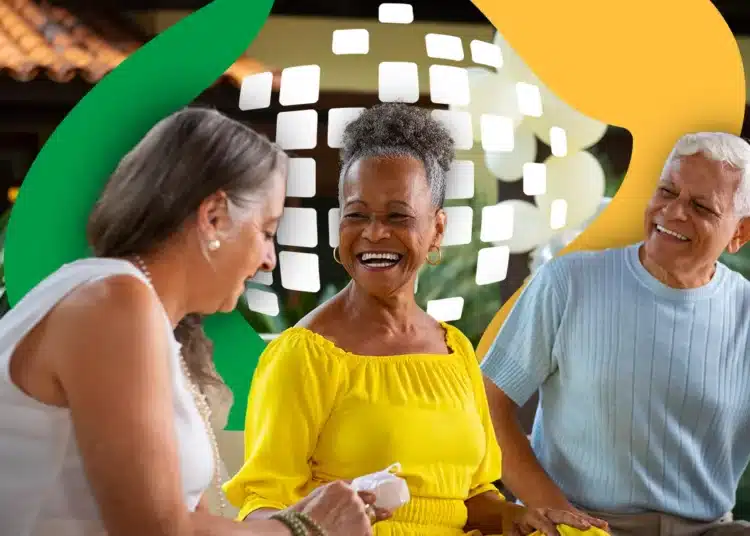 Três idosos sorrindo sentados juntos, com destaque para mulher de amarelo segurando papel