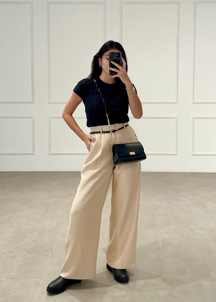 Look feminino com blusa preta justa, calça wide leg bege de alfaiataria com risca de giz e bota coturno preta de bico arredondado.