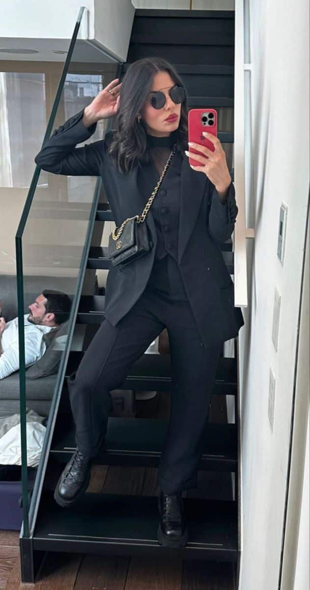 Mulher usando look total black com blazer estruturado, colete abotoado, calça de alfaiataria reta e bota coturno de couro preta.