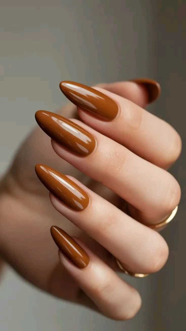Mão com unhas longas decoradas em esmalte caramelo brilhante, transmitindo elegância