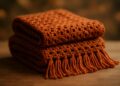 Peças de crochê dobradas em tom terracota sobre mesa de madeira