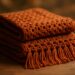 Peças de crochê dobradas em tom terracota sobre mesa de madeira