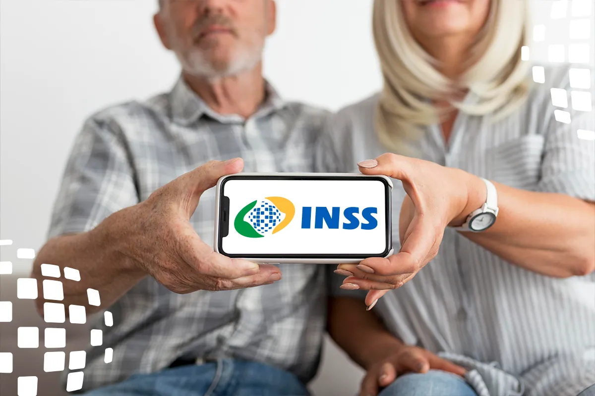 Um casal de idosos, de forma desfocada ao fundo, segura um smartphone em primeiro plano. Na tela do celular, aparece em destaque o logotipo oficial do INSS.