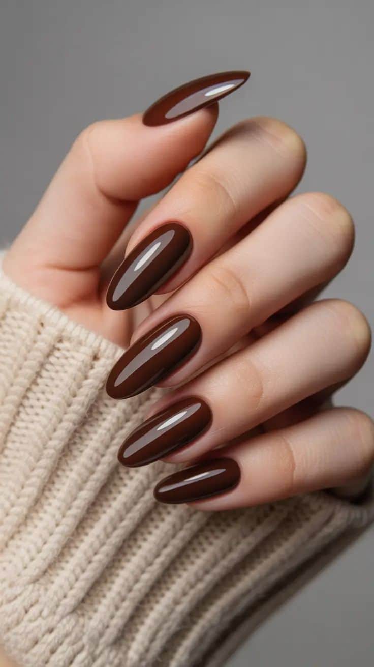 Mão feminina exibe unhas longas ovaladas esmaltadas em marrom chocolate glossy