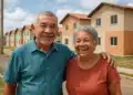 Casal de idosos abraçados sorrindo diante de conjunto habitacional recém-construído
