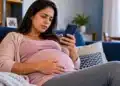 Mulher grávida em repouso no sofá consulta o celular, representando o pedido de auxílio-doença pelo Meu INSS.