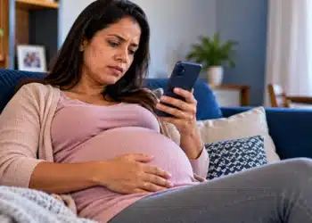 Mulher grávida em repouso no sofá consulta o celular, representando o pedido de auxílio-doença pelo Meu INSS.