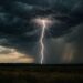 Raio caindo sobre campo aberto com nuvens escuras e chuva intensa ao fundo