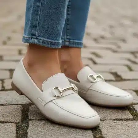 Mulher usando mule sem salto branco com calça jeans em piso de pedra