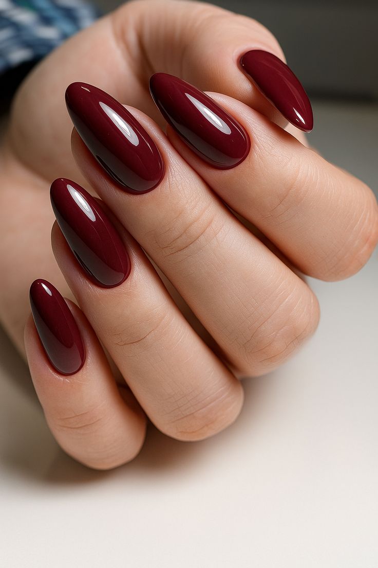 Mão feminina com unhas longas esmaltadas em vinho profundo e acabamento brilhante