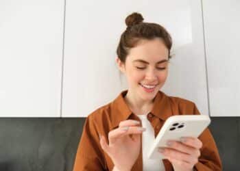Mulher sorrindo interagindo com smartphone branco em ambiente interno