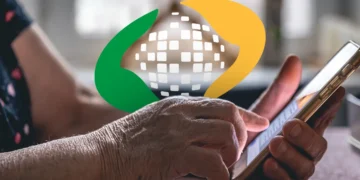Close das mãos de uma pessoa idosa segurando um smartphone e navegando no aplicativo oficial. Sobre a imagem, o logotipo colorido do INSS (Previdência Social) em destaque.