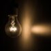 Uma lâmpada incandescente acesa em um ambiente escuro, emitindo uma luz amarelada que projeta um feixe lateral.