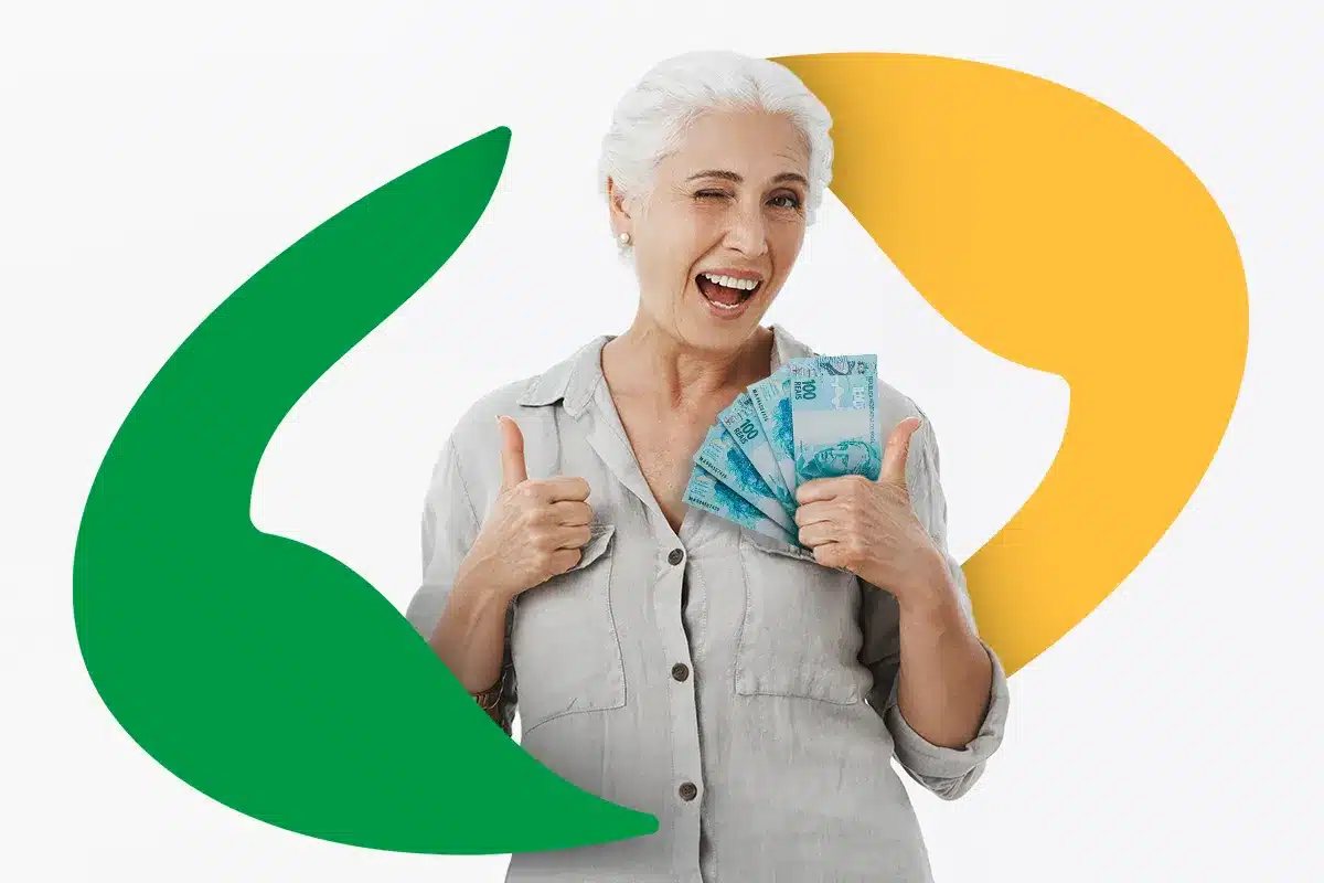 Uma mulher idosa sorridente, com cabelos brancos, piscando para a câmera. Ela segura um leque de notas de 100 reais (reais brasileiros) em uma das mãos e faz um sinal de "joinha" (thumbs up) com ambas as mãos. O fundo é branco e possui dois grandes elementos gráficos em forma de folha ou balão nas cores verde e amarela.