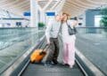 Casal de idosos tirando selfie em aeroporto com mala de viagem representando acesso a passagens aéreas baratas