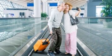 Casal de idosos tirando selfie em aeroporto com mala de viagem representando acesso a passagens aéreas baratas