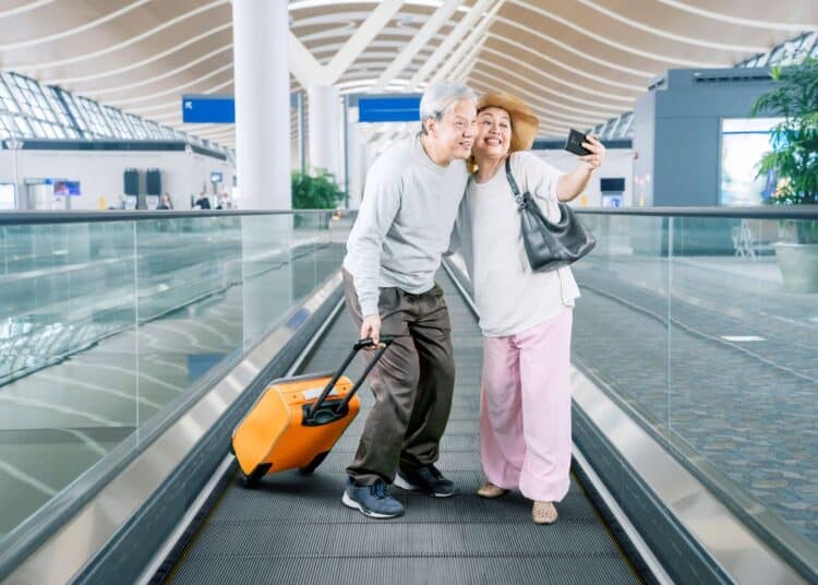 Casal de idosos tirando selfie em aeroporto com mala de viagem representando acesso a passagens aéreas baratas