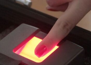 Dedo com esmalte vermelho pressionado em leitor biométrico com luz vermelha
