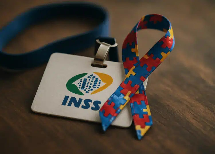 Crachá do INSS sobre mesa de madeira ao lado de laço colorido com peças de quebra-cabeça simbolizando o autismo