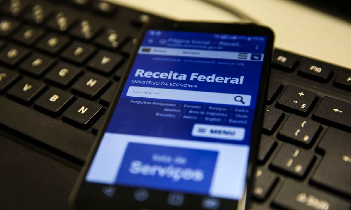 Celular exibindo site da Receita Federal sobre teclado de computador