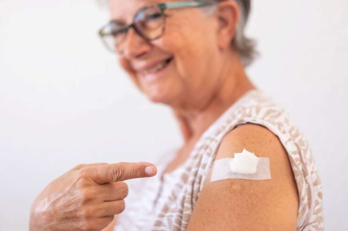 Idosa sorrindo apontando para curativo no braço após vacinação