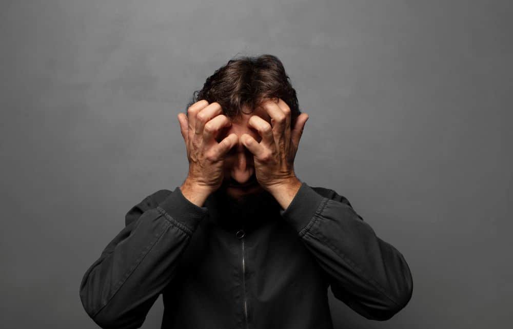 Homem com as mãos na cabeça, expressão de confusão mental e sofrimento, ilustrando quando o autodiálogo compulsivo afeta a saúde emocional.