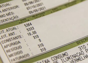 Close em uma conta de luz mostrando detalhes de leitura de consumo, medidor de kWh e descrição de taxas de iluminação pública e bandeiras tarifárias.
