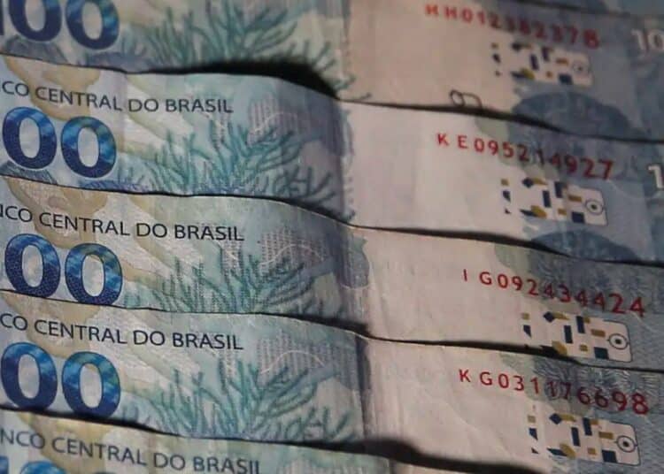 Várias cédulas de 100 reais brasileiros empilhadas com foco nos detalhes de segurança e no número cem.