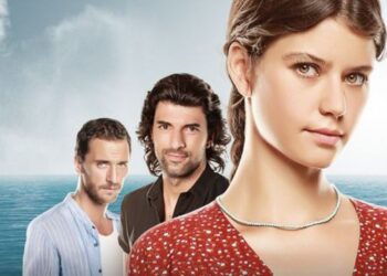 Uma foto de elenco da novela turca Fatmagül, com três personagens principais em primeiro plano. Uma jovem mulher com longos cabelos castanhos e vestido vermelho está à direita, olhando para a frente. Atrás dela, dois homens turcos com expressões sérias: um com cabelo escuro e camisa preta, e outro com cabelo mais curto e camisa listrada. O fundo é um vasto oceano azul sob um céu nublado, com a linha do horizonte visível.